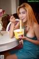 A woman in a blue dress eating a bowl of noodles.