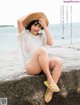 A woman sitting on a rock by the ocean wearing a straw hat.