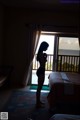 A woman standing in front of a window looking out at the ocean.