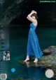 A woman in a blue dress standing on a rock in the water.