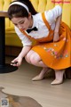 A woman in an orange dress crouching down looking at her cell phone.