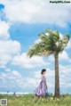 A woman in a purple dress walking in a field next to a palm tree.