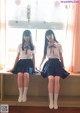 Two young women sitting on a window sill in school uniforms.