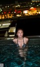 A woman in a black bikini sitting in a swimming pool.