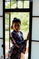 A woman in a black and pink kimono standing by a window.